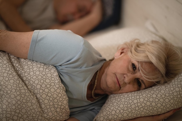 Mulher acordada na cama durante a noite enquanto o parceiro dorme, sem conseguir desligar a cabeça