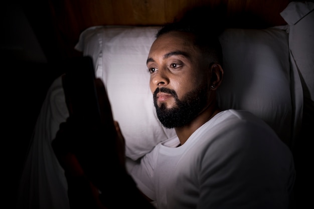 Homem deitado no escuro com o rosto iluminado pelo celular, hábito que dificulta parar de pensar na hora de dormir