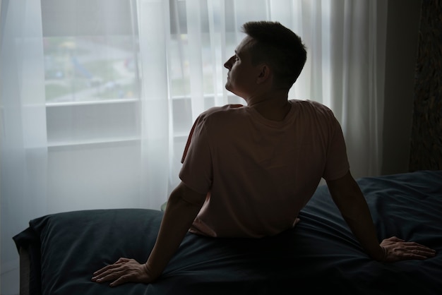 Homem sentado na beira da cama à noite, olhando para a janela, cena comum de quem procura tratamento para mente acelerada